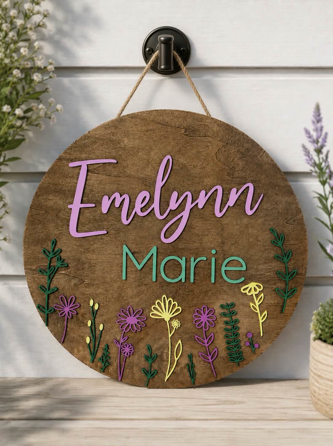 Round painted nursery sign reading Emelynn Marie with wildflowers
